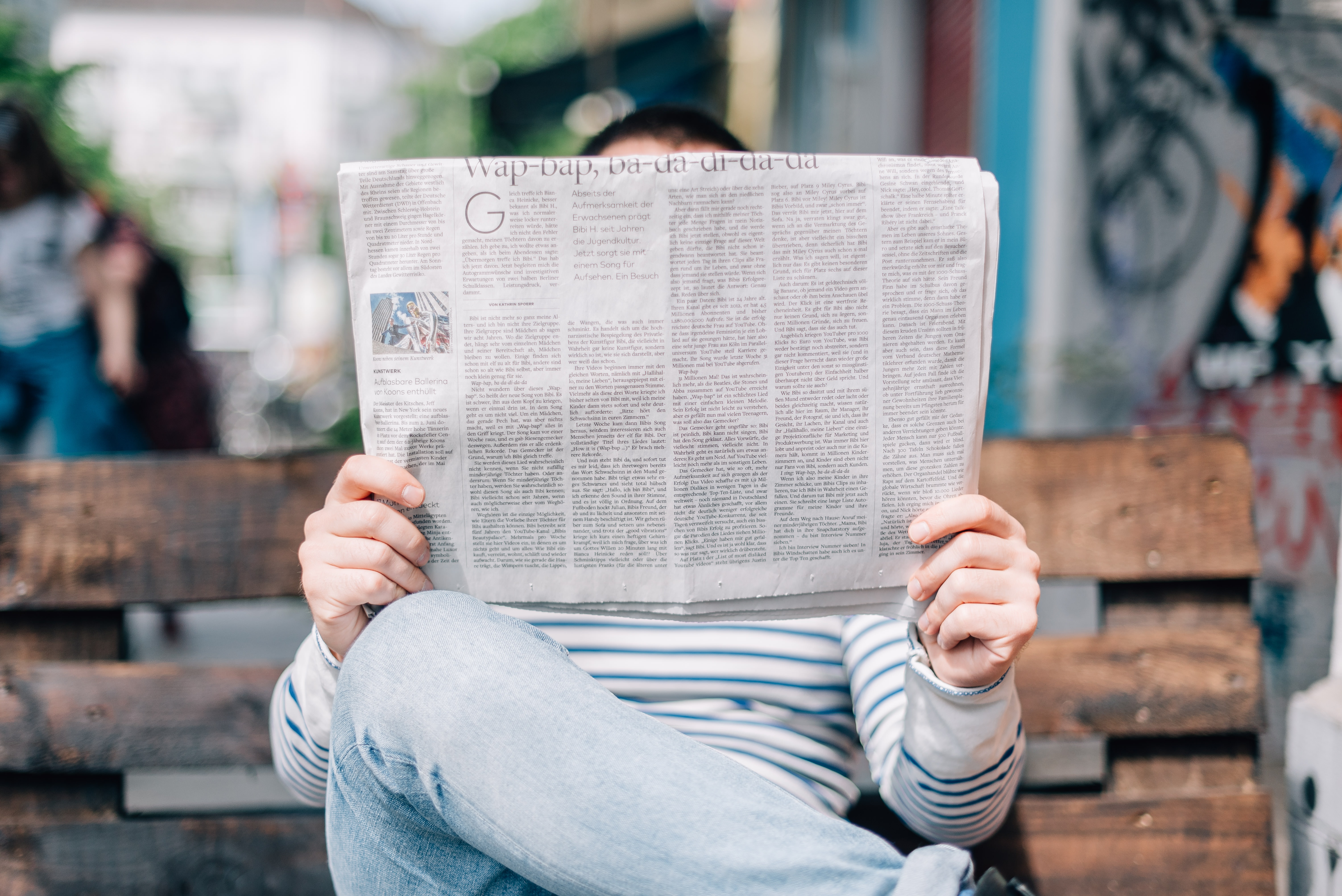 Person sitzt auf einer Bank und liest Zeitung