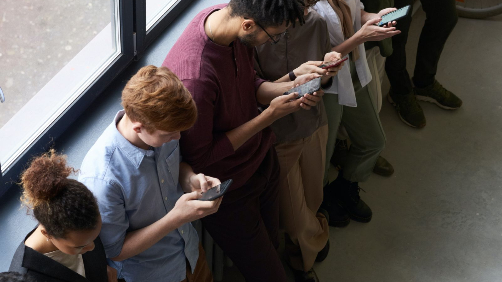 aufs Smartphone guckende Menschen am Fenster