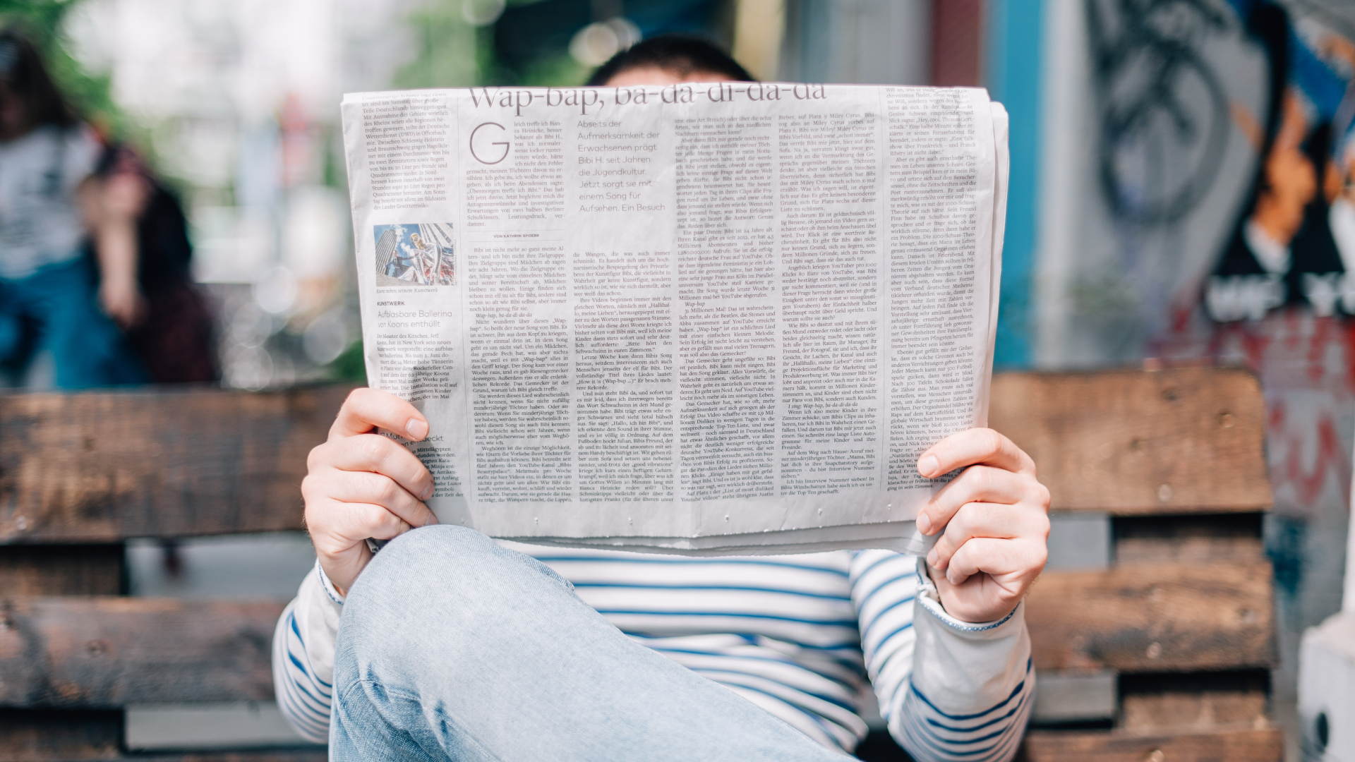 Person sitzt auf einer Bank und liest Zeitung