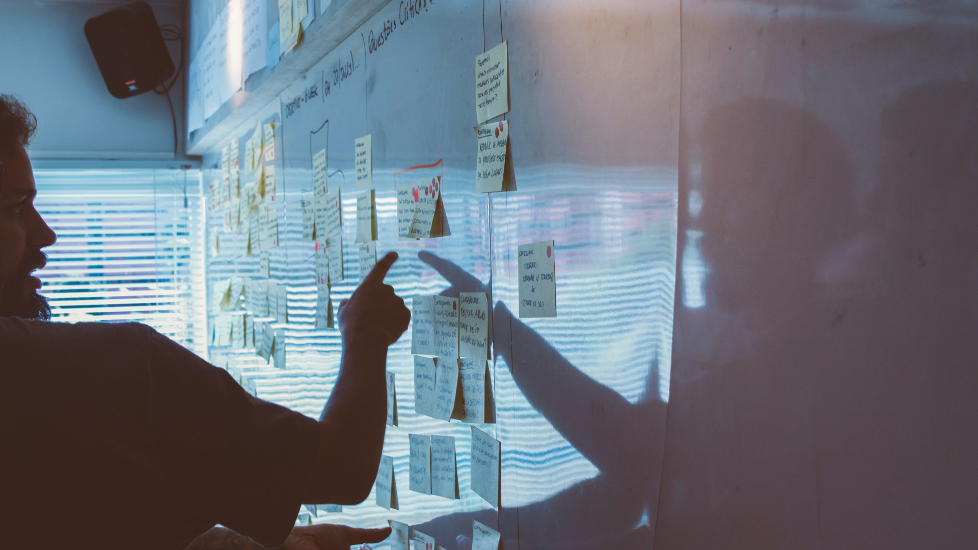 Eine Person steht vor einem Whiteboard, an dem mehrere Post-its kleben.