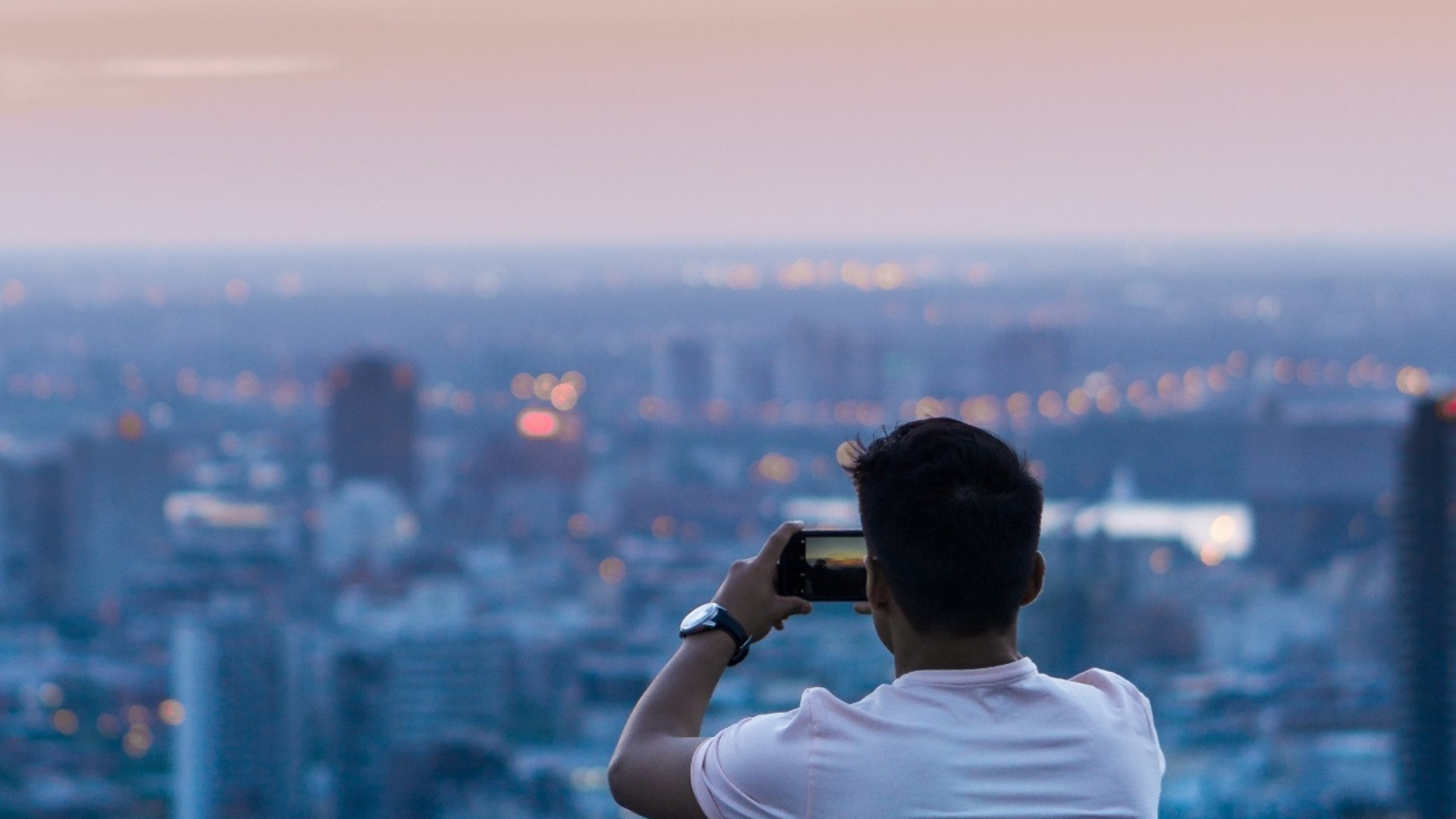 Mann fotografiert die Skyline einer Stadt mit seinem Smartphone.