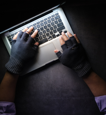  Hände in fingerlosen Handschuhen tippen am Laptop, dunkle Atmosphäre 